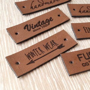 Puede incluir: Seis etiquetas de cuero marrón con texto negro. Las etiquetas dicen "handmade", "handknitted", "Vintage since 1920", "Winter Wear", "Finch & Smith" y "Fusion Collection".