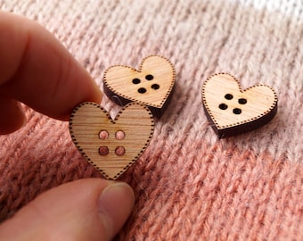 May include: Three wooden heart-shaped buttons with brown edges and a light brown center. Each button has four small holes in the center.