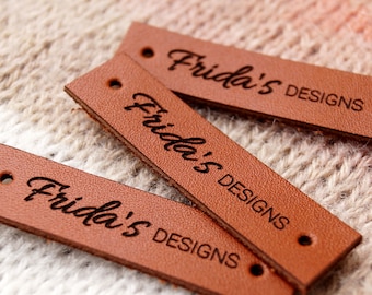 May include: Three brown leather labels with the text "Frida's Designs" engraved on them.