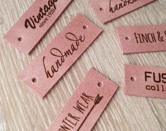 May include: Five pink leather labels with different text. The labels are for clothing and accessories. The text on the labels includes "Vintage since 1920", "handmade", "Winter Wear", "handknitted", and "Finch & Co."