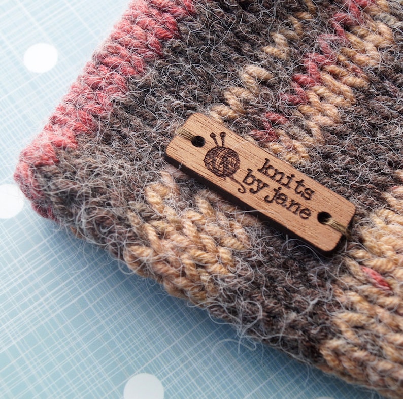 May include: A close-up of a brown, beige, and pink knitted fabric with a wooden tag that reads "Knits by Jane".
