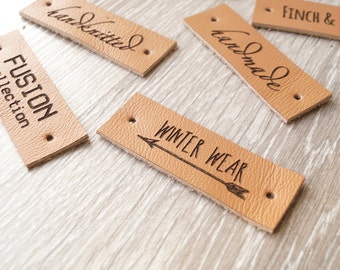 May include: Six brown leather labels with different text. The labels are rectangular and have holes punched in the corners. The text on the labels includes "Fusion Collection", "Hand Knitted", "Handmade", "Winter Wear" with an arrow, "Finch &", and "Vintage".
