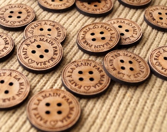 May include: Wooden buttons with the text "FAIT A LA MAIN PAR MARIA" in French, meaning "Handmade by Maria". The buttons are brown and have a heart shape in the center.