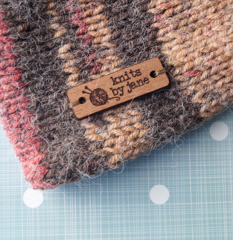 May include: A brown and beige knitted hat with a wooden tag that says "knits by jena".