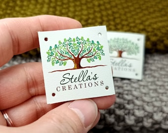 May include: White square leather tag with a green tree illustration and the text "Stella's Creations" in black cursive font. The tag has four holes punched in the corners.