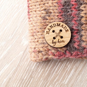 May include: A close-up of a brown and red knitted fabric with a wooden button that says "Handmade by Kim".
