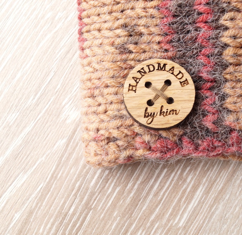 May include: A close-up of a brown and red knitted fabric with a wooden button that says "Handmade by Kim".