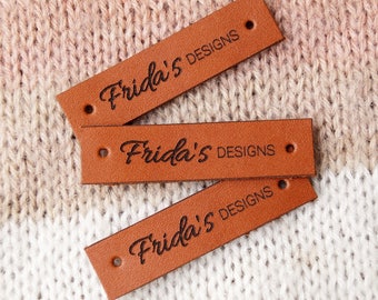 May include: Three brown leather labels with the text "Frida's Designs" embossed in black.