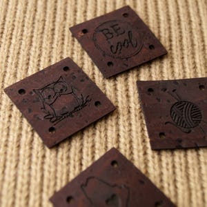 May include: Four brown cork fabric patches with different designs. The designs include an owl, a ball of yarn with knitting needles, a circle with the text "BE COOL" inside, and a design that is not clear.