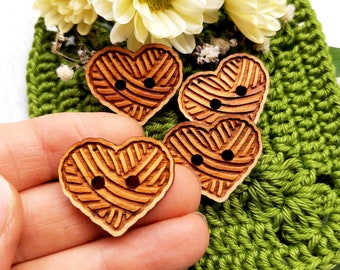 May include: Four wooden heart-shaped buttons with a yarn pattern and two holes each. The buttons are brown and have a natural wood finish.
