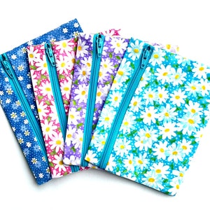 May include: Four zippered pouches with a daisy print. The pouches are in shades of blue, pink, purple, and light blue. The zippers are turquoise.