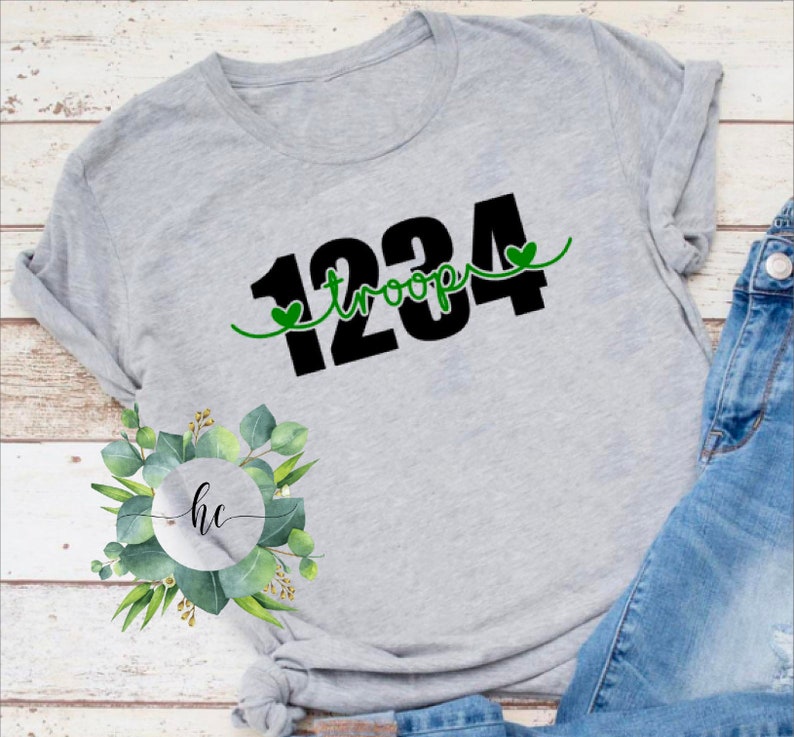 Puede incluir: Camiseta gris con texto negro que dice "1234 troop" con un coraz&oacute;n verde a cada lado del texto.