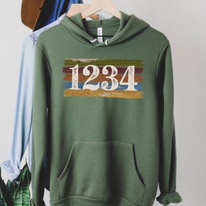 May include: A green hooded sweatshirt with a white graphic of the number 1234 on a colorful striped background.