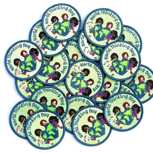 May include: A pile of round, green and blue embroidered patches with the text "World Thinking Day" and a graphic of children holding a globe.