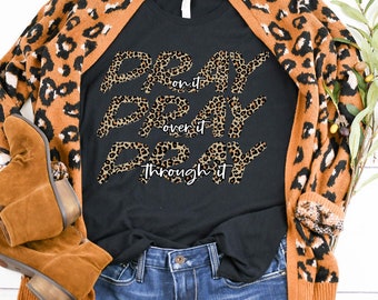 May include: Black t-shirt with a leopard print design that says "Pray on it, Pray over it, Pray through it". The shirt is paired with a brown leopard print cardigan and blue jeans.