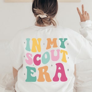 May include: White sweatshirt with the text "IN MY SCOUT ERA" in colorful retro letters.