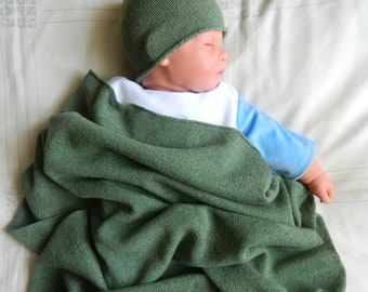 May include: A green knitted baby blanket with a baby wearing a green knitted hat and a blue and white shirt sleeping on a white and brown patterned surface.