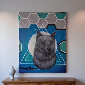 Pode incluir: Uma pintura em tela com a cabeça de um lobo cinzento contra um fundo azul com formas geométricas. O lobo está centrado, com um círculo branco atrás. A obra de arte é exibida numa parede branca acima de um armário de madeira.