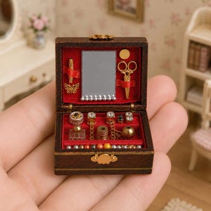 May include: A miniature wooden jewellery box with a red velvet interior. The box contains a small mirror, tiny scissors, and various miniature jewellery pieces. The box is brown with gold accents and is open, revealing the contents.