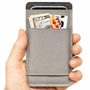 May include: A gray phone wallet with a pocket containing a fifty-dollar bill and several cards. The wallet is held in a hand, showcasing its slim design and functionality. The top of the wallet is a dark gray felt material.