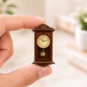 May include: A miniature brown wall clock with a rectangular frame, ornate top detailing, and a round cream-colored face. The clock features black numerals, decorative hands, and a small gold-toned pendulum. The text "SWEET HOME" is printed on the face.