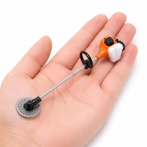 May include: A miniature string trimmer replica featuring a bright orange engine housing, a white fuel tank, a long silver metal shaft, a black circular handle, and a small silver circular cutting blade with a perforated pattern at the base.