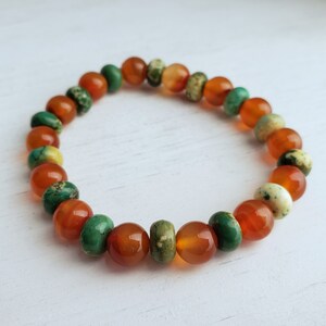 Puede incluir: Un brazalete hecho de cuentas de cornalina, turquesa y jaspe. Las cuentas son una mezcla de naranja, verde y blanco.