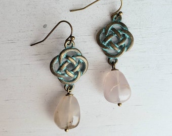 May include: A pair of earrings with a Celtic knot design in antique brass with a turquoise patina. Each earring features a teardrop-shaped pink stone.