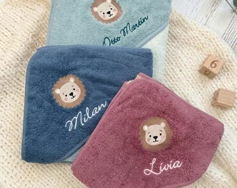 May include: Three hooded baby towels in sage green, navy blue, and dusty rose. Each towel features an embroidered lion face and a personalized name: Otto Martin, Milan, and Livia, stitched in a cursive font on the corner hood.