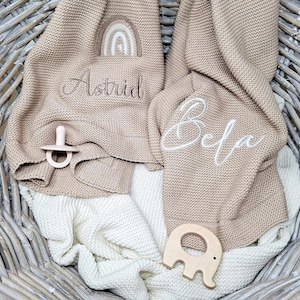 Gestrickte Babydecken mit Namen und Motiv bestickt. Eine mit "Astrid" und einem Regenbogen bestickt, die andere Babydecke ist mit dem Namen "Bela" bestickt.