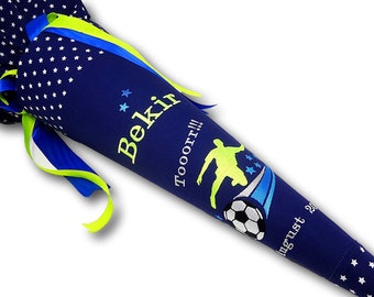 Peut inclure: Un cône scolaire bleu et blanc avec un motif de joueur de football et le nom "Bekir" et le texte "Tooor!!!" en jaune. Le cône a un ruban vert et bleu.
