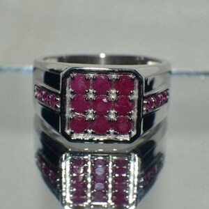 May include: A silver ring with a square-shaped ruby gemstone set in the center. The ring is adorned with smaller ruby gemstones around the center stone and along the band.