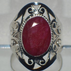 May include: A silver ring with an oval-shaped ruby gemstone set in a filigree design.