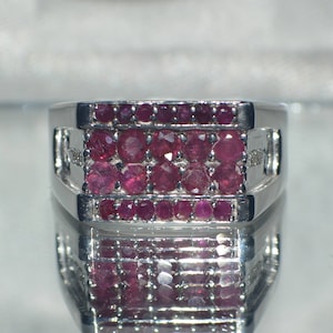 May include: A silver ring with a rectangular setting featuring three rows of small, red ruby stones.