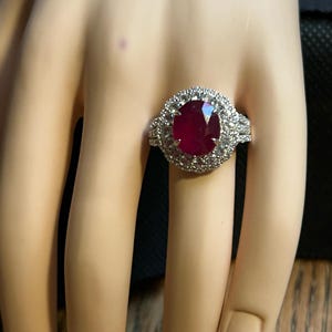 May include: A ring with a large oval ruby surrounded by a halo of smaller diamonds. The ring is set in white gold.