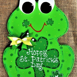 May include: Green frog-shaped wooden door hanger with a shamrock design and the text "Hoppy St. Patrick's Day".
