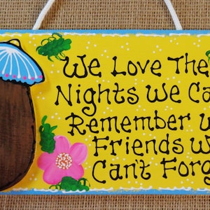 May include: A yellow wooden sign with a painted coconut drink and the text "We Love The Nights We Can't Remember With Friends We Can't Forget!"
