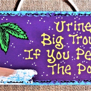 May include: A purple wooden sign with a painted palm tree and ocean waves. The sign reads "Urine Big Trouble If You Pee In The Pool!"