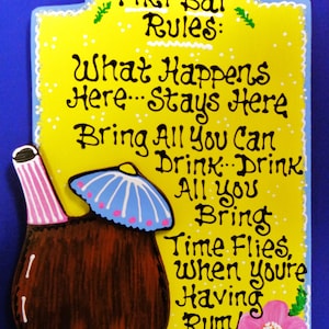 May include: A yellow wooden sign with white polka dots and blue trim. The sign has a hand-painted tiki bar with a blue and white umbrella and the text "Tiki Bar Rules: What Happens Here...Stays Here Bring All You Can Drink: Drink All You Bring Time Flies, When You're Having Rum!"