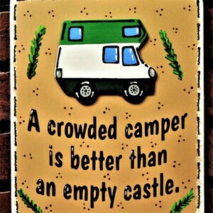 May include: A brown wooden sign with a white border and a white camper van illustration. The sign has the text "A crowded camper is better than an empty castle."