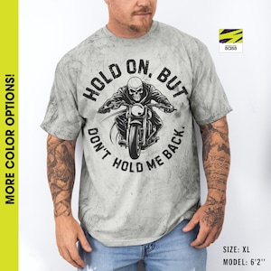 以下が含まれることがあります： くたびれた感じのグレーのTシャツで、白黒の骸骨がバイクに乗っているグラフィックが描かれています。グラフィックには「Hold On. But Don't Hold Me Back.」というテキストが含まれています。