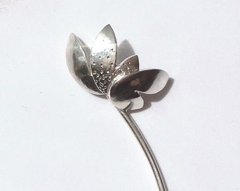 Puede incluir: Un broche de plata con forma de flor con un tallo largo y delgado. La flor tiene cinco pétalos y una superficie texturizada.