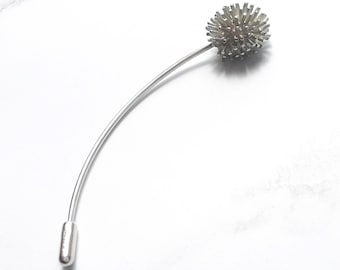 Puede incluir: Un broche de plata con forma de diente de león con un tallo largo y una cabeza de flor redonda y texturizada.