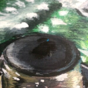 May include: A close-up of a black and silver painted metal lid with a blue dot in the center. The lid is surrounded by a green and white abstract background.