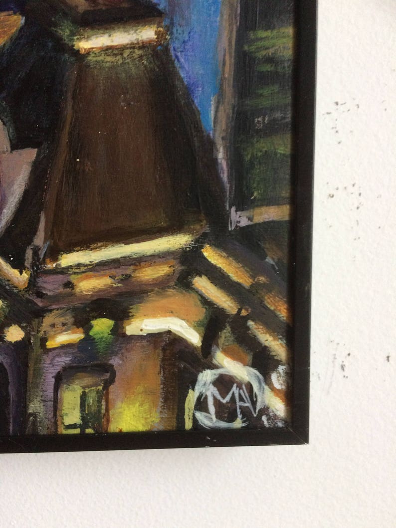 May include: A framed painting of a city scene with buildings in shades of brown, yellow, and green. The painting is signed "MAV" in the lower right corner.