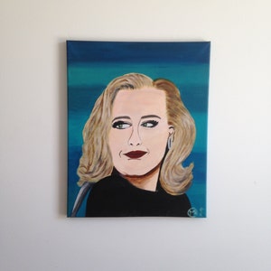 May include: A portrait painting of a woman with blonde hair and dark red lipstick. She is wearing a black top and has a turquoise and blue background. The painting is on a canvas and is mounted on a white wall.