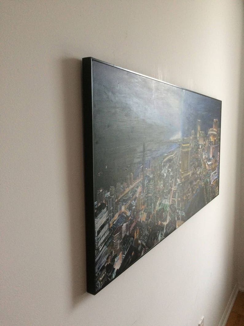 May include: A framed canvas print of a city skyline at night. The city is lit up with lights and the sky is dark with clouds. The print is in a black frame.