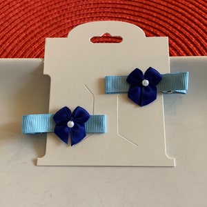 Königsblaue Minischleifen, die an hellblauem Bändchen gesäumt sind, zieren kleine Krokodilklemmen. Haarspangen Paar. Schleifenband, kleine Schleifen