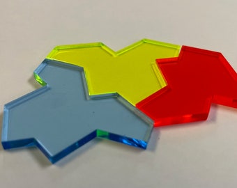 Może przedstawiać: Cztery kolorowe, przezroczyste elementy gry w kolorze niebieskim, żółtym i czerwonym. Każdy element ma unikalny kształt geometryczny z karbowanym wzorem. Elementy są ułożone na białej powierzchni, tworząc atrakcyjny wizualnie układ.