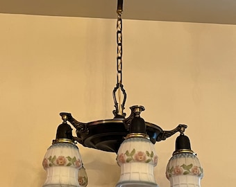 May include: A black and gold chandelier with five frosted glass shades featuring a floral design. The shades are bell-shaped and have a white and blue pattern.